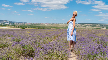 Smiling woman in a lilac field looking at the camera sunglasses stands smiling stands