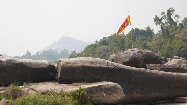 Yellow and red flag waving in the wind among large boulders in nature near the village of Hampi, Karnataka state
