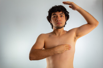 Young naked hispanic man with wavy hair and shaved beard, doing a checkup on his chest for signs of breast cancer