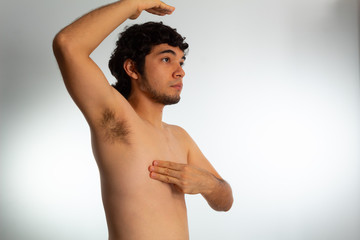Fototapeta na wymiar Young naked hispanic man with wavy hair and shaved beard, doing a checkup on his chest for signs of breast cancer