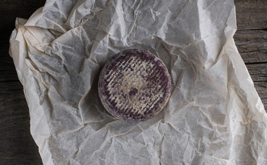 Close up of soft French cheese with purple crust on paper.flat lay