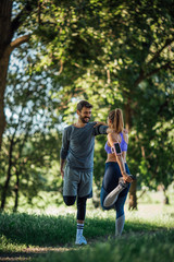 Side image of a young couple doing warming exercise in nature, they smiling and stick each other to maintain balance