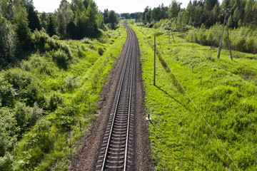 Long winding train track surrounded by green fields and trees and a high-voltage electrical grid