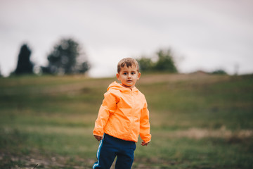 Boy in a yellow jacket stands on a meadow and looks away on a gloomy day