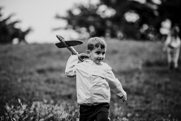 Black and white image of a boy stands alone in the meadow and holding a toy airplane in his hand