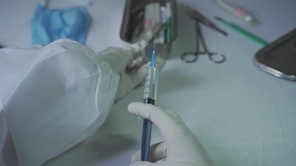 top view of a medical doctor drawing out covid 19 vaccine into a syringe at her work table.