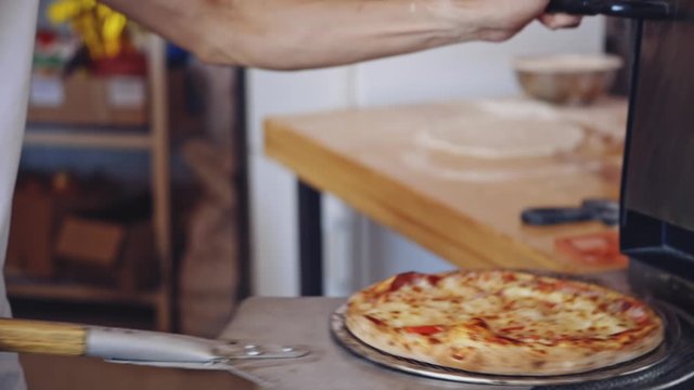 Hot delicious pizza. Pizzeria master takes out ready pizza from the oven. Chef is pulling out fresh pizza with a special pizza spatula in the kitchen.