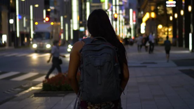 A young female tourist walking along the streets of Tokyo at dusk in summer.