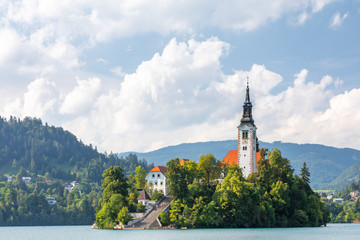 Close up of the iconic Slovenian island on the lake Bled surrounded by trees and vegetation, under...