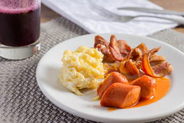 Café da manhã de hotel com bacon, salsicha, ovos mexidos, suco de uva