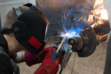 Welder wearing a mask and gloves repairs a car