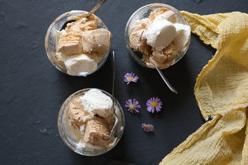 Ice cream in three glass bowls on a dark table.

