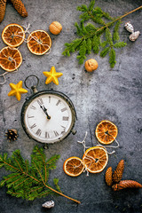 Christmas clock composition. Vintage clock surrounded by fir branches, cones, dried oranges, Christmas tree decorations on a dark background. Top view, copy space, flat lay