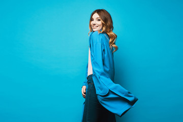 Side view of a model girl in a long blue cardigan isolated at the blue background with a copy space