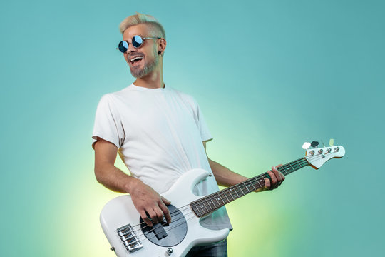 Cheerful hipster man play white bass guitar in neon lights. Rock music concept. Rock star.