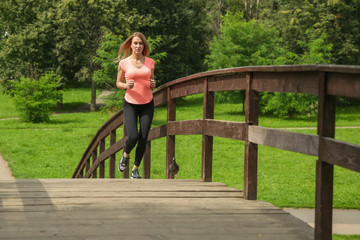 Naklejka na ściany i meble young sport woman running across the bridge in the park