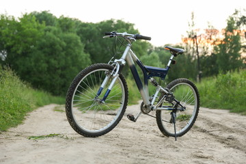 Naklejka na ściany i meble beautiful mountain bicycle is on sand road on green nature background at sunset