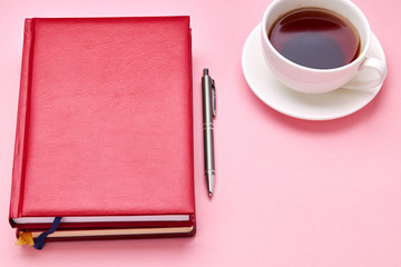 above view for pink desk with red diary and tea cup on it. office workplace background backdrop
