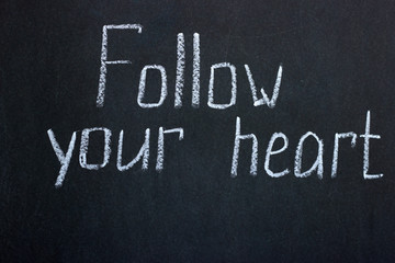 
White chalk lettering on a dark board Follow your heart. Motivating phrase