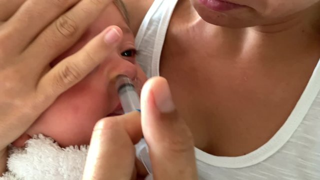 Mother removing baby mucus. Toddler congested nose