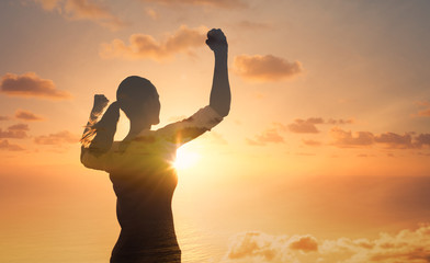 Young female against sunrise with fist in the air feeling strong and confident. Victory and success concept.	
