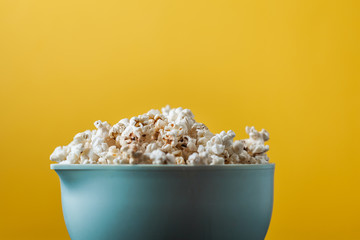 Cheesy popcorn in the blue bowl on the yellow background