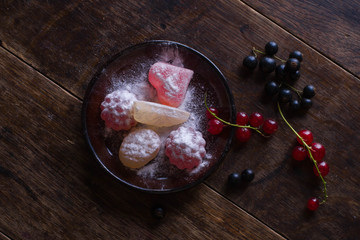 Black plate with figured colorful marmalade and currant on the old wooden table