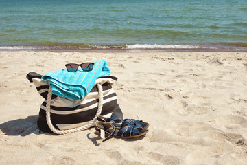 Set of personal belongings lying on the beach sand with calm sea in background in bright summer day