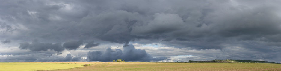 Storm clouds over the fields. Landscape at sunset. Tragic gloomy sky. Panorama. The sun is hidden.