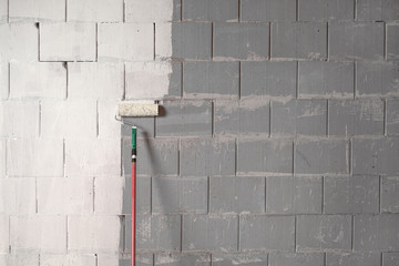 Roller is painting a rough wall of grey stones with white paint, background concept for...