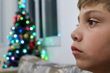 Retrato de uma parte do rosto de um menino com as luzes de uma árvore de Natal atrás sem foco