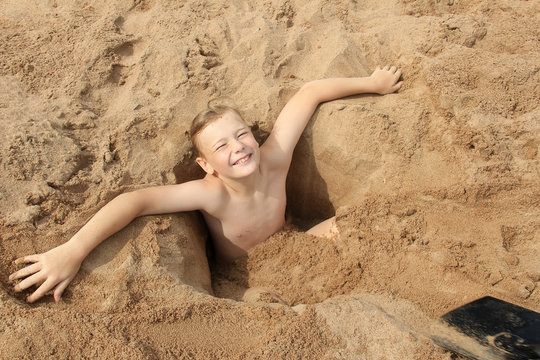 Child is buried in the sand on the beach.