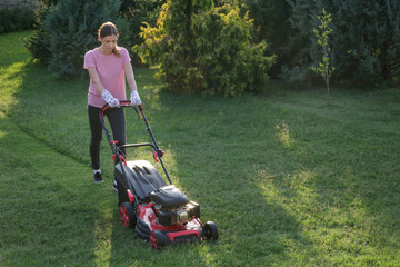 Young woman cutting grass with a lawn mower. Outdoor household chores concept.