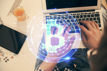 Double exposure of man's hands typing over computer keyboard and crypto currency theme hologram...