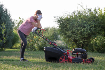 Tired woman making a short break while cutting grass with a lawn mower. Outdoor household chores...