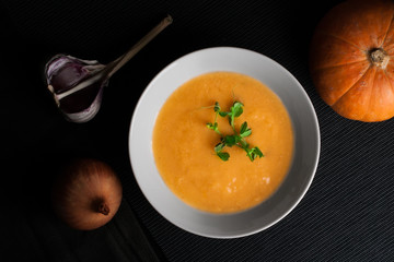 Pumpkin soup with ingredients on the dark background.