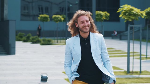 Young prosperous start-up developer young businessman with curly hair and smile walking happily out office enjoyiing working day finished. Business person. Expressioins. Success.