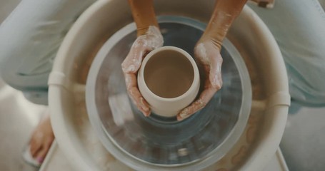 Woman makes clay bowl in studio on pottery wheel, up-close hands and clay, top view, handmade - Powered by Adobe