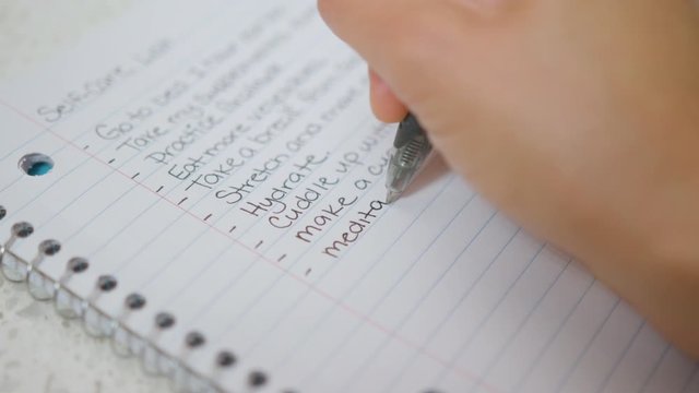 Woman's hand writing "meditate" on a self-care list. Close up.