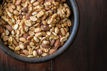 Mix of seeds, walnut, peanuts and almonds in a bowl on wooden table.
