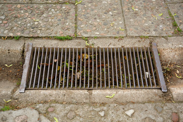 High angle shot of a rusty metal rain drain on a sidewalk