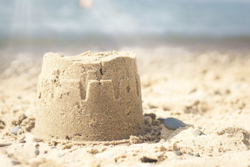Closeup of a small sandcastle at the beach under the sunlight with a blurry background