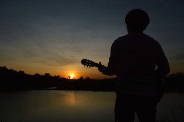 Black man silhouette standing playing guitar In front there was a sunset and a river. Evening nature
