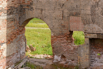Old walls of red brick ruins. Arched passage. Broken brick fragments. Green grass. Concept of the ruins of a medieval building, manor.