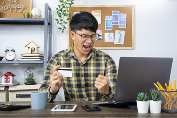 Asian man holding credit card to Online shopping with laptop computer and entering security code, internet banking or work from home consumer commerce concept.
