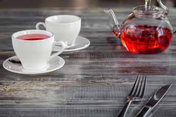 Pink berry red teapot, white cups, cutlery on gray wooden background