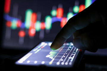 Businessman finger touching screen on smartphone with stock market graph at night.