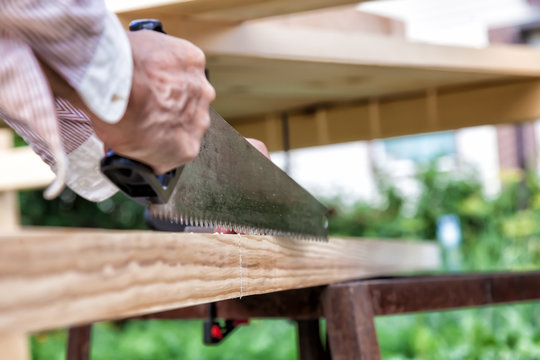 A hand-held metal saw with a black plastic handle with sharp teeth in the hands of a carpenter when sawing wooden beams with small chips flying to the sides. on a summer day.