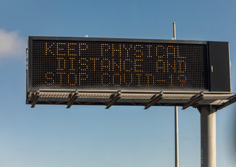 Freeway sign stating Keep Pysical Distance Stop Covid-19 against a blue sky