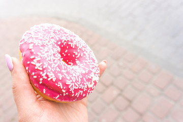 Pink doughnut in a girl's hand with copy space. donut with a pink chocolate frosting. Sweet dessert festive. Breakfast and bachelorette party concept.